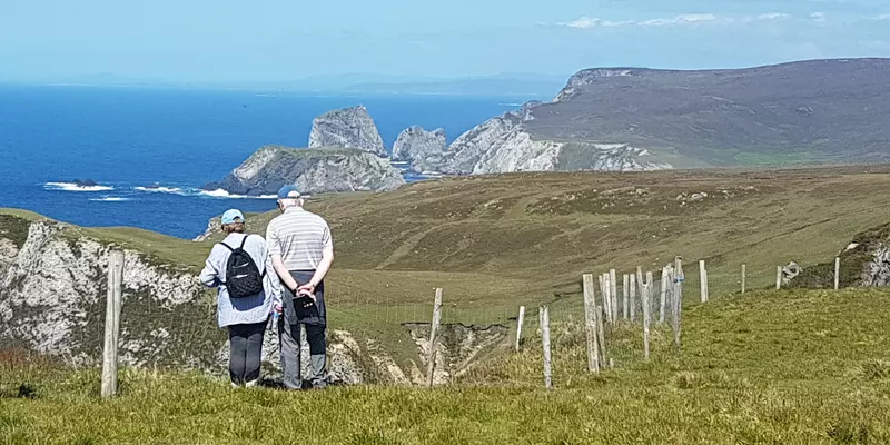 Hikers standing near fence along rocky coast.