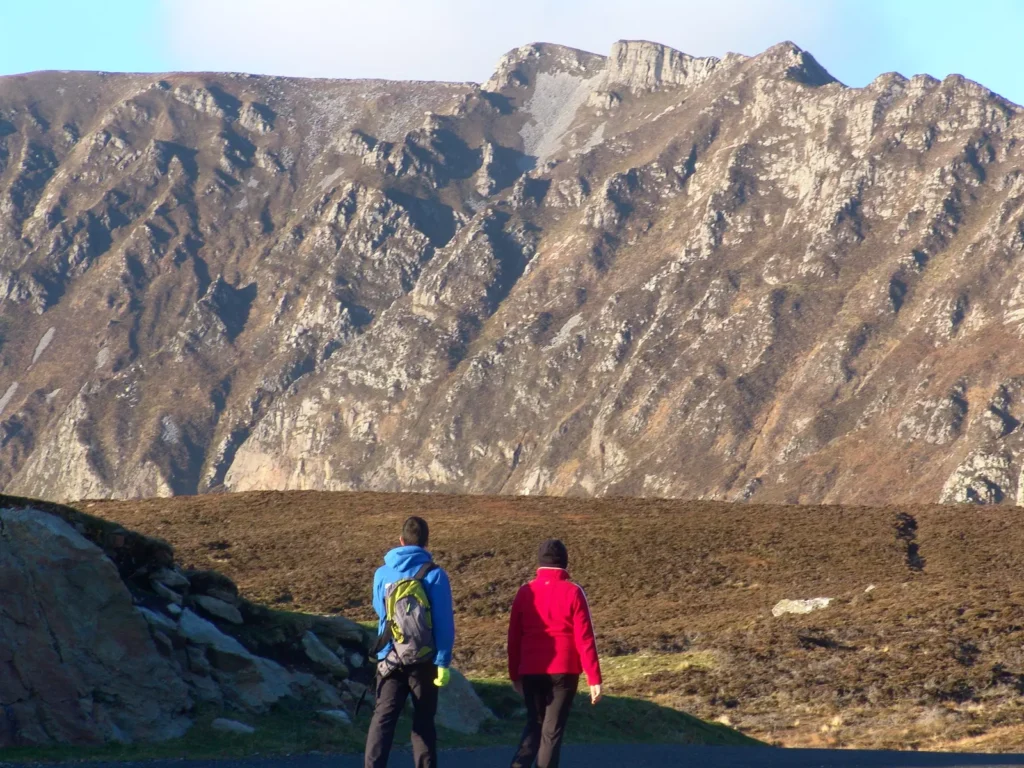 Two hikers walking near steep mountain side.