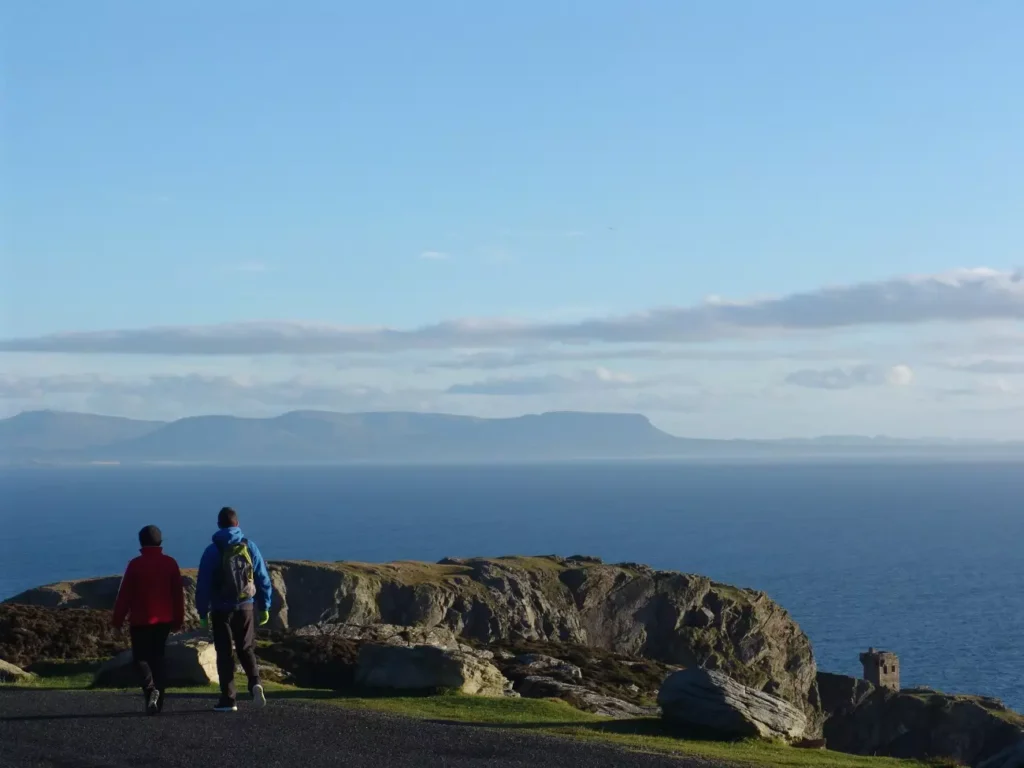 Two hikers walking high above sea with mountains in the distance.
