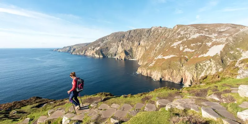 Hiker with walking poles on high ground above ocean.
