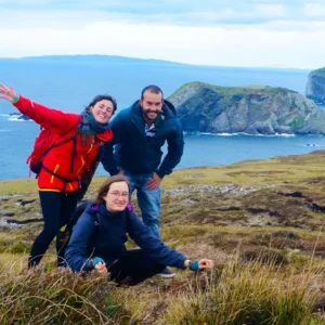 Group of 3 hikers with one sitting along rocky coastline.