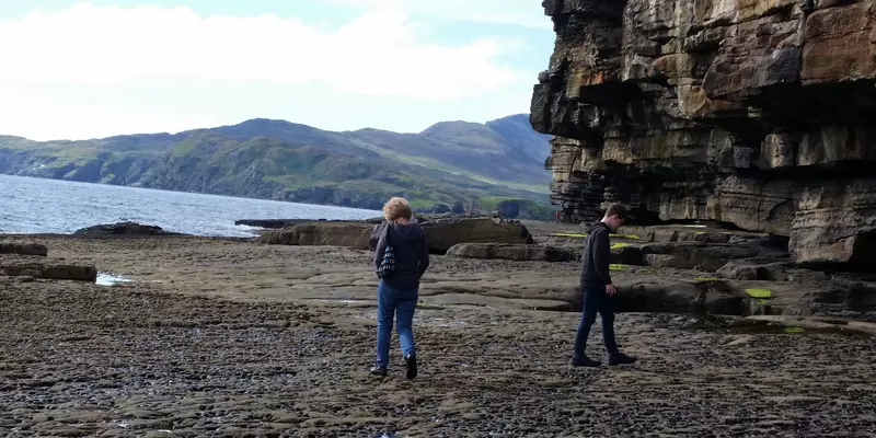 Two people walking on rocky shoreline.