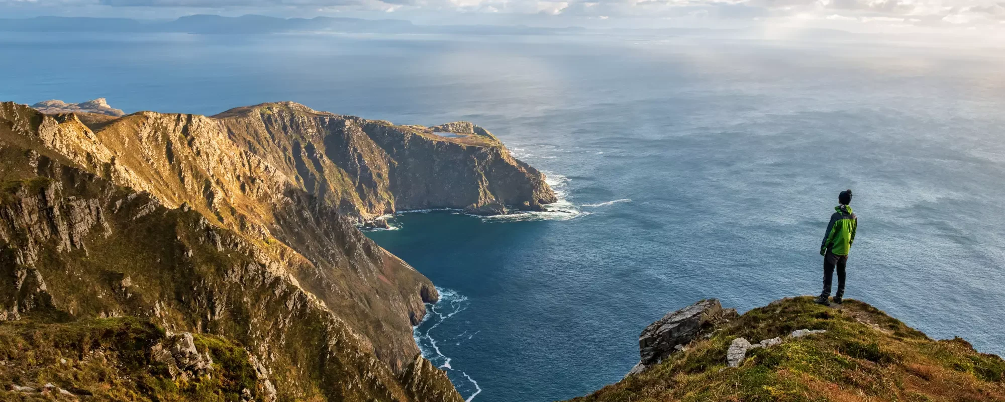 Hiker standing on cliff overlooking the coast.